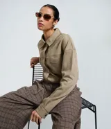 Camisa de corte regular confeccionada en gamuza sintética color beige, con cuello inglés, cierre frontal abotonado, mangas largas con puños ajustados y bolsillo tipo cargo en el pecho.