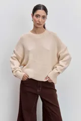 Sweater de punto en color beige, con cuello redondo acanalado, mangas largas con puños ajustados y diseño holgado.