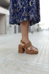 Sandalias de cuero color marrón con plataforma y taco ancho. Tienen dos tiras anchas sobre el empeine y una tira con hebilla al tobillo.