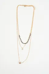 Collar multicapa de cadena fina dorada. Presenta tres niveles: uno con pequeñas cuentas negras, otro con un dije circular transparente y un tercero con un dije en forma de estrella.