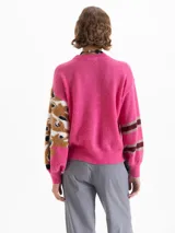 Sweater de punto color fucsia, con cuello redondo. Presenta un diseño de manchas abstractas en tonos marrón, negro y blanco en el frente y en la manga derecha. La manga izquierda tiene un diseño de rayas horizontales en tonos marrón y gris.