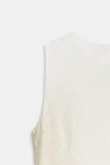 Vestido corto sin mangas, color blanco roto o crema, confeccionado en tejido de encaje. Presenta un bajo con volante asimétrico que cae en cascada hacia un lado.