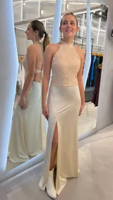 Vestido largo beige, con cuerpo de cuello halter bordado con motivos florales y falda fluida con abertura frontal en la pierna.