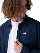 Camisa de manga larga de popelina color azul marino, de corte clásico con cuello camisero, cierre frontal con botones y bolsillo en el pecho con etiqueta de la marca Caterpillar. Incluye sistema para convertir las mangas en cortas.