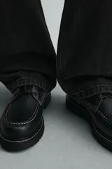 Zapato de cordones tipo derby, color negro, con capellada de cuero, horma redonda y suela con volumen. Presenta detalle de pespuntes blancos a contraste.