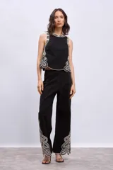 Blusa negra sin mangas, de corte recto y escote redondo, con detalles de bordados contrastantes en color blanco en los bordes y costados.