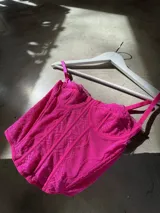 Corset o top estilo bustier color fucsia, con tirantes finos y detalles de encaje o tejido calado. Presenta un escote festoneado y un corte ajustado que termina en pico en la parte inferior.