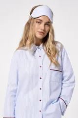 Pijama de dos piezas de algodón a rayas celestes y blancas, compuesto por una camisa de manga larga con botones y ribetes marrones, y un pantalón largo de corte recto con elástico en la cintura.