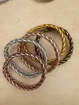 Pulsera de resina flexible con diseño trenzado y acabado brillante, con relleno de lámina metálica en tonos dorados, plateados y cobrizos.