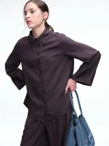 Camisa de corte oversize color bordó, con cuello clásico, cierre frontal de botones y mangas largas amplias con puños anchos. Presenta un diseño de caída fluida con bajo redondeado y levemente más largo en la parte posterior.