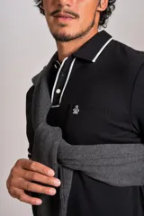 Polo de manga corta confeccionado en tejido interlock suave, color negro con detalles de vivos en color blanco en el cuello y las mangas. Presenta tapeta con botones y un bolsillo frontal con el logo bordado.