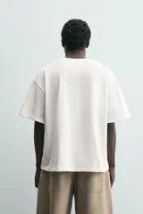 Camiseta de corte relajado confeccionada en algodón, con cuello redondo y manga corta. Presenta un estampado artístico de una flor a trazo grueso en color negro sobre fondo blanco.