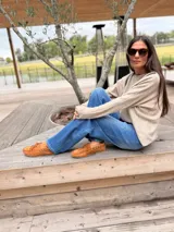 Sweater de tejido de punto en color beige, con corte holgado y diseño de cuello redondo. Presenta apliques decorativos de cuero en la parte frontal superior, formando un detalle geométrico.