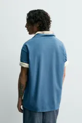 Polo de algodón con estructura piqué, color azul deslavado. Presenta un corte regular fit, cuello solapa con cierre de botones, manga corta con acabado en rib y bajo asimétrico con aberturas laterales.
