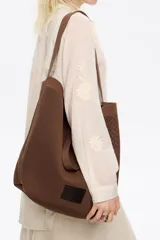 Bolso shopper de estructura blanda y gran tamaño, confeccionado en tejido técnico tipo mesh. Cuenta con doble asa de hombro, cierre mediante cordón ajustable y etiqueta de cuero con logo grabado en la parte frontal.