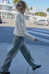 Blazer corto blanco de cuello solapa y manga larga con hombreras. Presenta un cierre frontal cruzado con dos botones dorados.