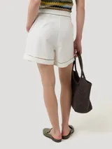 Short de tiro medio confeccionado en mezcla de lino orgánico y viscosa, color beige. Presenta diseño con pinzas frontales, bolsillos laterales y detalles de calados decorativos en la cintura y en el ruedo.