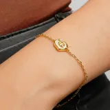 Pulsera dorada con cadena de eslabones finos y dije ovalado con el signo zodiacal de Cáncer en color blanco.
