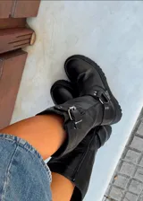 Bota de caña alta confeccionada en cuero vacuno encerado, con diseño de estilo biker. Presenta detalles de hebillas metálicas niqueladas en la caña y cierre lateral. Cuenta con suela de cuero artesanal y forrería vacuna en su interior.