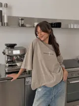 Remera oversize de color marrón topo con efecto acid wash, cuello redondo y manga corta. Cuenta con un pequeño estampado gráfico frontal con el texto 'WAKE UP IND' y una calavera.