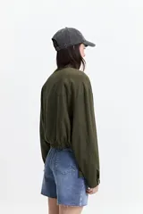 Campera verde militar sin cuello, con elástico y cinto regulable en la cintura, bolsillos amplios y cierre frontal.
