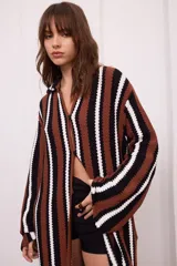 Saco largo tejido a crochet con rayas verticales en colores marrón, negro y blanco. Tiene cuello tipo camisa, mangas acampanadas y cierre frontal con botones.