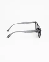 Lentes de sol de montura gruesa color negro, estilo cuadrado/rectangular. Poseen cristales tintados en color ámbar/beige claro. Presentan detalles metálicos (remaches) en las esquinas superiores del frente.