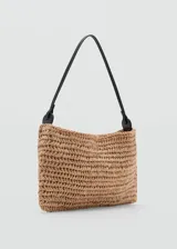 Bolso tipo cartera de mano de fibras naturales trenzadas en color tostado, de tamaño pequeño, con asa de hombro delgada de color negro y cierre magnético interior.