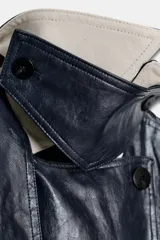 Trench oversize de efecto piel color azul marino, con cuello solapa, manga larga, bolsillos delanteros y cinturón ajustable del mismo tejido. Cierre frontal cruzado con botones y forro interior.