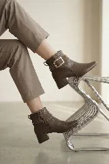 Bota corta de cuero con taco cuadrado bajo y punta redondeada. Presenta una tira decorativa en el tobillo con una hebilla metálica rectangular. Cuenta con cierre lateral interno para facilitar el calce.