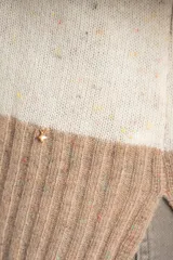 Sweater de punto con diseño de rayas horizontales anchas, alternando color beige camel y blanco roto con motas de color. Presenta cuello redondo y puños y borde inferior acanalados.
