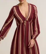 Vestido largo evasé de Marfinno, confeccionado en mezcla de viscosa y lino, con diseño de rayas verticales en tonos bordó y beige. Presenta escote en V, busto ajustado y mangas largas abullonadas con puños elastizados.