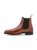 Bota tipo Chelsea de cuero color marrón, con paneles laterales elásticos en color negro y tirador en la parte trasera. Presenta una suela plana con pequeño tacón.