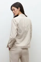 Blazer sastrero color beige melange confeccionado en lino, con solapas clásicas y cierre frontal abierto.