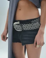 Short de jean negro con terminaciones desflecadas y cinturón de cuero negro con argollas plateadas.