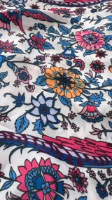 Vestido largo con estampado floral y de aves en tonos rojizos y azules sobre fondo crema. Presenta escote halter profundo en V y cintura marcada con falda con vuelo en capas.