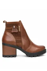 Bota de cuero color marrón de caña corta, con taco alto y ancho, suela dentada negra y paneles laterales elásticos con textura de punto. Incluye una placa metálica lateral con el logo de la marca y detalle de etiqueta de cuero en el talón.