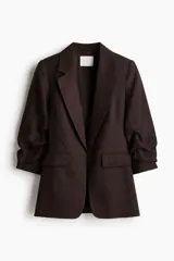 Blazer entallado de color marrón, con hombreras, solapas de muesca, mangas tres cuartos fruncidas y bolsillos delanteros con solapa. Diseño sin cierre y totalmente forrado.