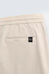 Pantalón tipo jogger de corte slim fit, confeccionado en tejido de algodón con elasticidad. Presenta cintura elástica ajustable con cordón, bolsillos frontales, bolsillos traseros de vivo y bajos con puños elásticos.