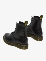Botas de caña media Dr. Martens modelo 1460, color negro con acabado liso. Presentan cierre de cordones con 8 ojales, suela de goma acanalada con cámara de aire, pespuntes amarillos característicos y tirador de talón con logo.