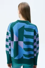 Sweater de tejido de punto con diseño geométrico multicolor en tonos verde, azul y lila. Presenta cuello redondo, mangas largas con puños acanalados y corte recto.