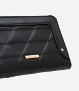 Billetera grande color negro, con cierre de cremallera perimetral y panel frontal acolchado con diseño de rombos. Presenta una placa metálica dorada en el centro y un dije colgante triangular dorado unido a la cremallera.