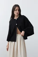 Saco tipo capa de punto color negro, con silueta fluida, corte amplio y cierre frontal con dos botones dorados.