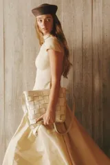 Cartera tipo morral de cuero color beige, con diseño trenzado artesanal, correa larga regulable y cierre superior.