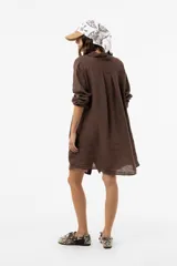 Vestido camisero de lino color marrón, de corte relajado, con cuello clásico, cierre frontal con botones, mangas largas regulables y bolsillos laterales.