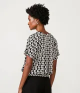 Blusa de viscosa con estampado geométrico en blanco y negro, escote de pico, manga corta y bajo elástico.
