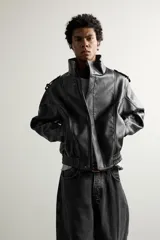 Cazadora biker relaxed fit confeccionada en tejido efecto piel, color negro. Cuenta con cuello subido, manga larga con puño ajustable y bajo elástico. Incluye bolsillos de vivo en la cadera y cierre frontal con cremallera oculta bajo una solapa diagonal con botones a presión.