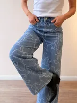 Jeans de corte wide leg y tiro alto, confeccionados en denim celeste con estampado de lazos en tono claro. Presentan cierre frontal con botón y cierre metálico, además de bolsillos funcionales.