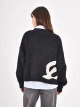 Cardigan de punto negro con diseño de sol en color tostado, cuello redondo y cierre frontal con botones. Presenta un tejido con motas de colores y corte holgado.