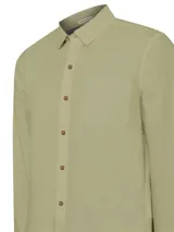 Camisa manga larga color verde oliva, confeccionada en popelina 100% algodón orgánico. Cuenta con cuello camisero, cierre frontal con botones de madera, bolsillo en el pecho con logo bordado y mangas ajustables con botones.